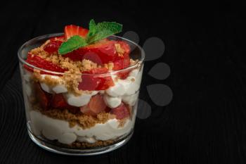 Strawberry with cookie and cream dessert decorated with mint leaf on black wooden background, with copyspace