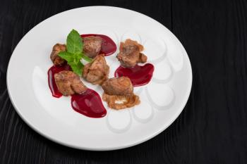 Delicacy Fried pork meat with zucchini puree and berries sauce decorated with mint on white plate on black wooden background