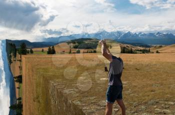 Man standing in in summer Altai mountains surreal landscape and holding circle mirror. Creative travel concept