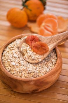 Oat flakes with  dried apricots at wooden plate on fruit background