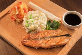 Grilled salmon with rice and vegetables at wooden table