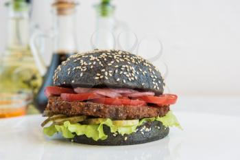 Black burger with beef meat cheese lettuce onion, tomato and sauce on white table