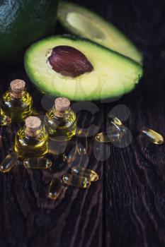 Oil of avocado with fish oil pills on a dark wooden background