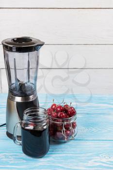 Cherry juice with glass jar,of berries, blender and juice on blue wooden background