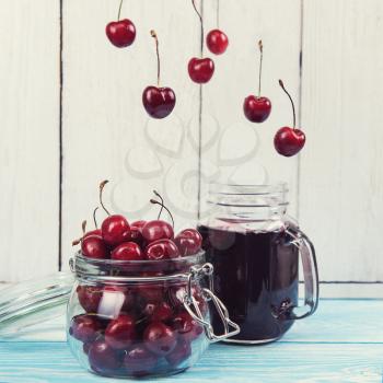 Cherry juice with glass jar of berries on blue wooden background