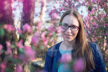 Portrait of young beauty woman in purple rhododendron flowers. Blooming rhododendron - maralnik in Altai mountain forest in the spring.