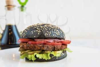 Black burger with beef meat cheese lettuce onion, tomato and sauce on white table