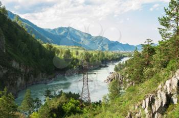 Power lines in the beautiful mountain landscape with a water stream in Altai, Siberia, Russia.