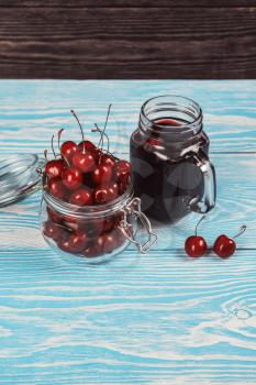 Cherry juice with glass jar,of berries, blender and juice on blue wooden background
