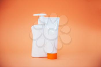 Different cosmetic bottles of cream, soaps, foams or shampoo on orange background.