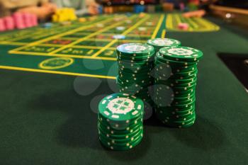 Casino, gambling and entertainment concept - stack of poker chips on a green table
