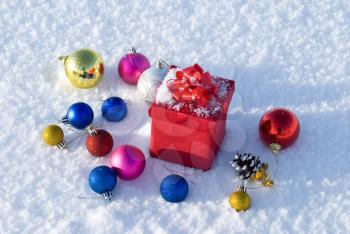 Red gift box on snow with christmas balls