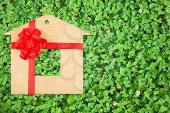Royalty Free Photo of a Background of a Bed of Green Clovers With a Symbol of a Home Made Out of Cardboard With a Red Bow and Ribbon