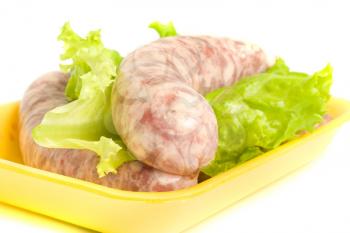 Closeup of one Uncooked Sausage on salad leaf over white