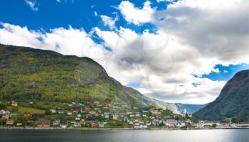 Mountains, village and Norwegian fiord. Blue sky with clouds