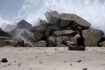 Royalty Free Photo of a Woman in the Lotus Position on the Beach With Waves Crashing Over the Rocks