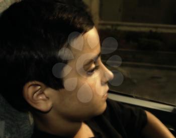 Boy with a sad facial expression, riding the bus at sunset, looking through the window.