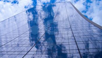 A photograph of the steel and glass skyscraper in New York City, dissolving into the sky above with clouds reflections.