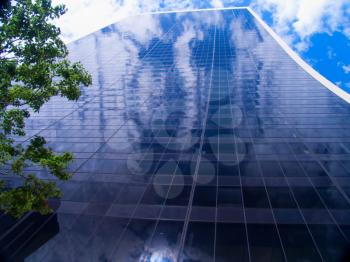 A photograph of the steel and glass skyscraper in New York City, dissolving into the sky above with clouds reflections.