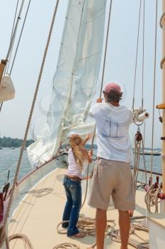 Girl helping a crew member to raise a sail on the private sail yacht.