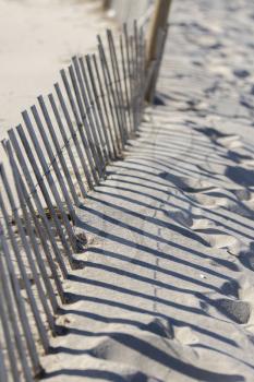 Wooden fence, grass and white sand dunes on the beach on a hot summer afternoon.