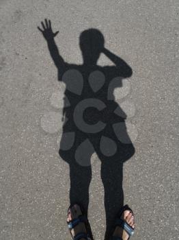 shadow of a man with a raised hand on the gray asphalt