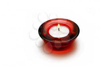 a burning candle in a round red glass candlestick on a white background