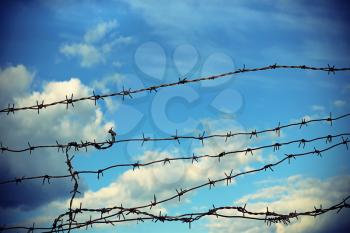 Barbed wire against blue sky with clouds