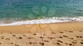 Rope with floats on the sea and sandy beach with footprints 