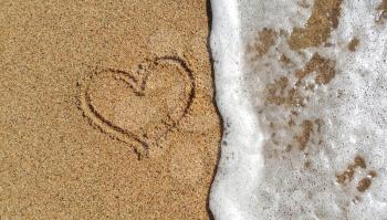 Heart drawing in the sand and sea foam on the beach