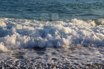 Sea waves and white foam in in the rays of the evening sun on the coast