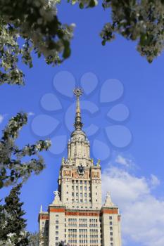 Moscow State University with symbolism of USSR against sky background with branch of flowering trees