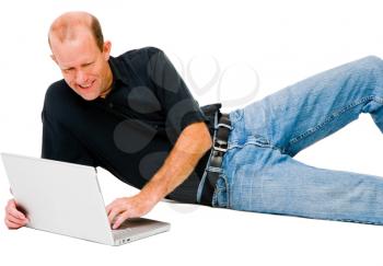 Smiling man lying and using a laptop isolated over white