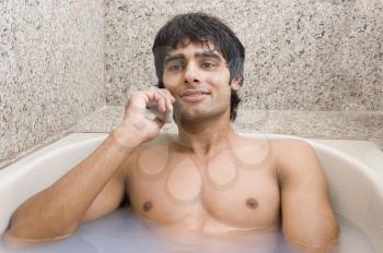 Man relaxing in the bathtub and talking on a mobile phone