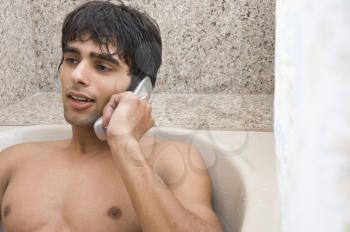 Man relaxing in the bathtub and talking on a mobile phone