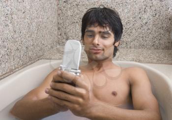 Man relaxing in the bathtub and text messaging on a mobile phone