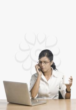 Businesswoman talking on a mobile phone in front of a laptop