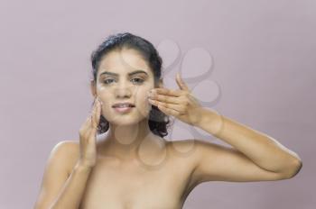 Portrait of a young woman applying moisturizer on her face