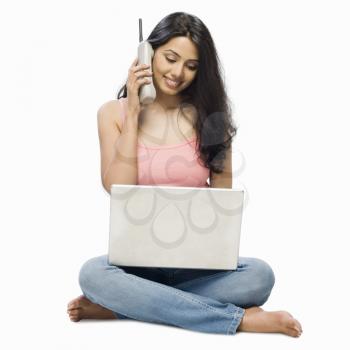 Young woman using a laptop and talking on a cordless phone