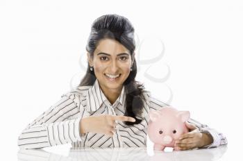 Portrait of a businesswoman pointing towards piggy bank