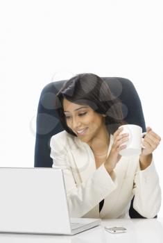 Businesswoman holding a coffee mug and looking at a laptop