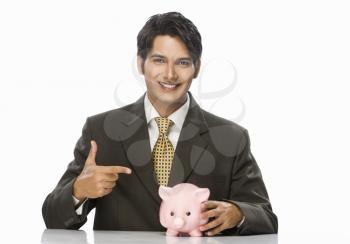 Portrait of a businessman pointing towards a piggy bank