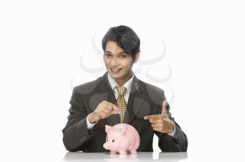 Portrait of a businessman pointing towards a piggy bank
