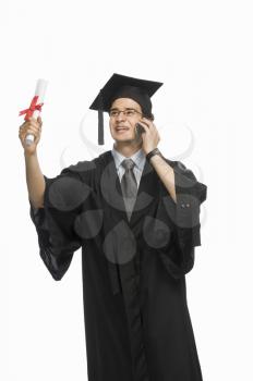 Happy male graduate holding his diploma and talking on a mobile phone