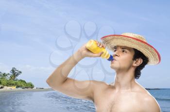 Man drinking water from a water bottle on the beach