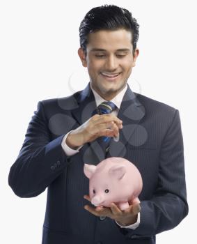 Businessman putting a coin into a piggy bank