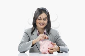 Businesswoman inserting a coin into a piggy bank