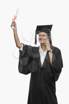 Graduate woman talking on a mobile phone and holding her diploma