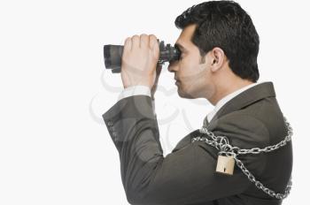 Businessman locked in chains and looking through binoculars