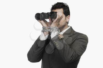 Businessman locked in chains and looking through binoculars
